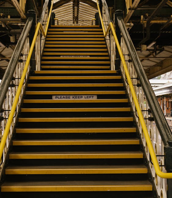 A black-and-white photograph showing an external emergency staircase attached to the side of a building, consisting of multiple landings connected by metal stairs with white railings. The staircases a